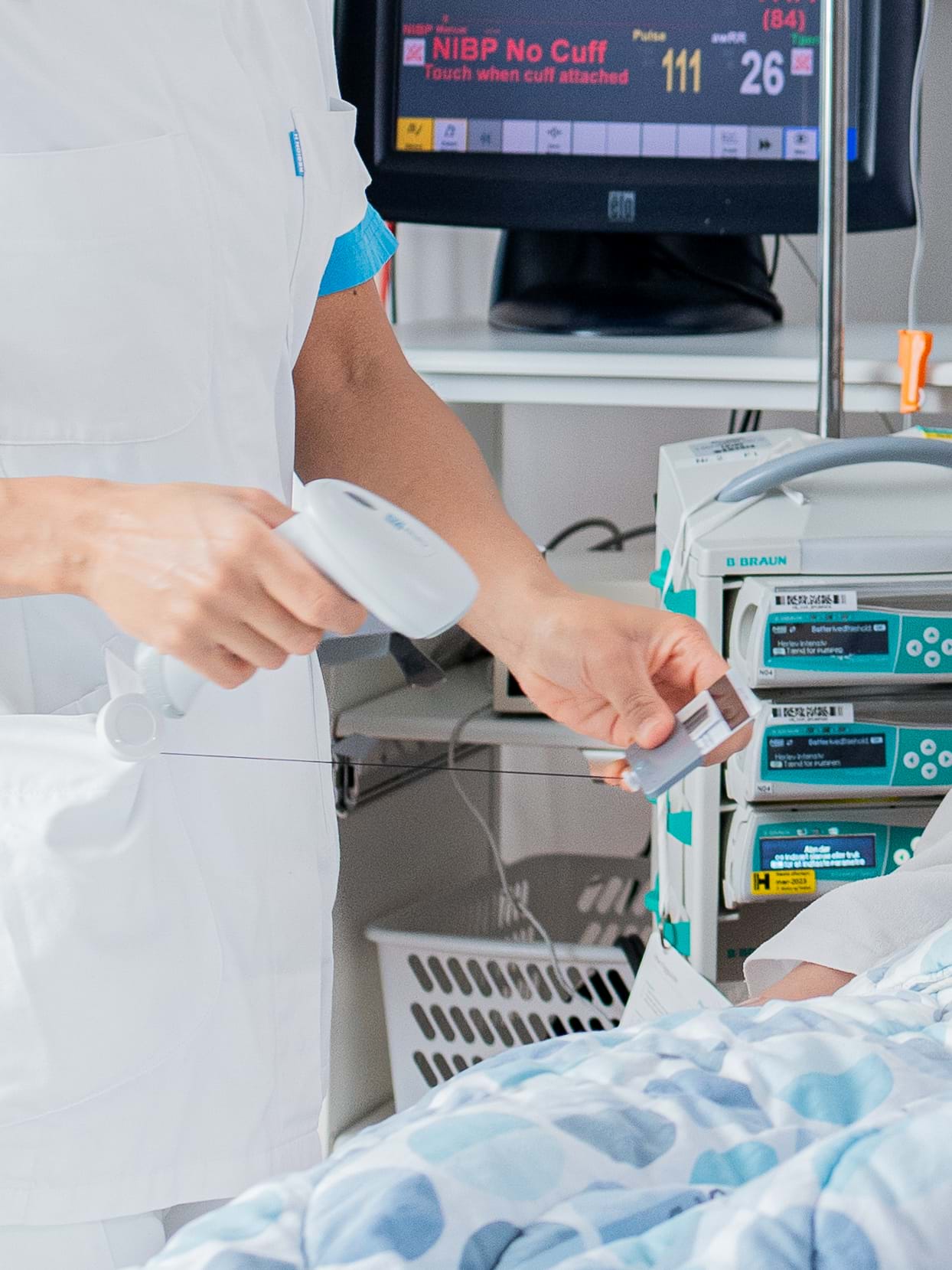 En helsearbeider i hvit uniform bruker en håndholdt strekkodeleser til å skanne et ID-kort ved siden av medisinsk utstyr.